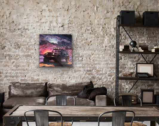 A square canvas wall art print depicting a rugged off-road vehicle on a colorful sunset mountain landscape, displayed on a rustic brick wall above a brown couch in a modern loft setting.