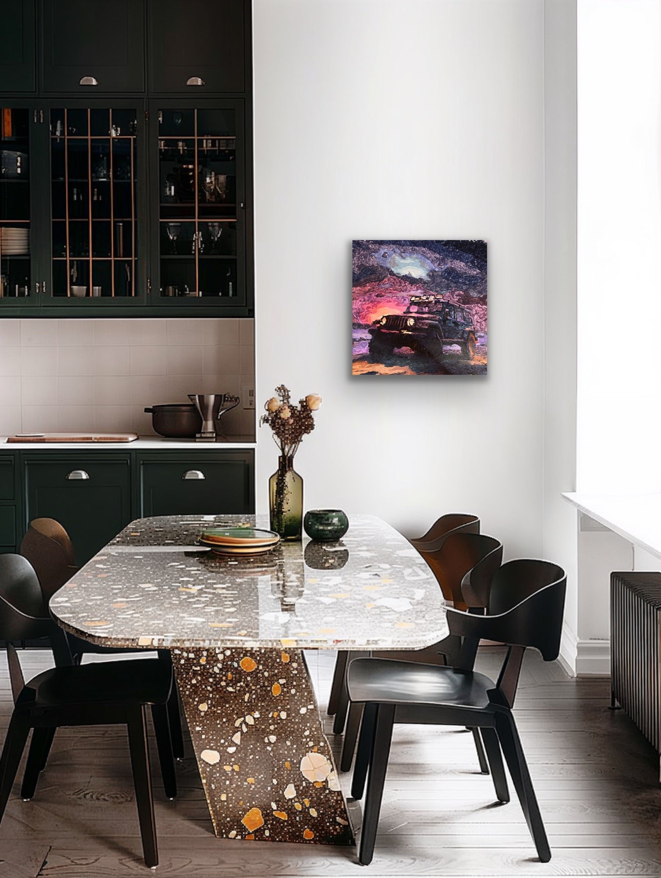 A modern dining room scene with a rectangular terrazzo-patterned table and black chairs, set in a contemporary kitchen. A square wall art print depicting a dark vehicle against a colorful sunset sky hangs on the white wall.